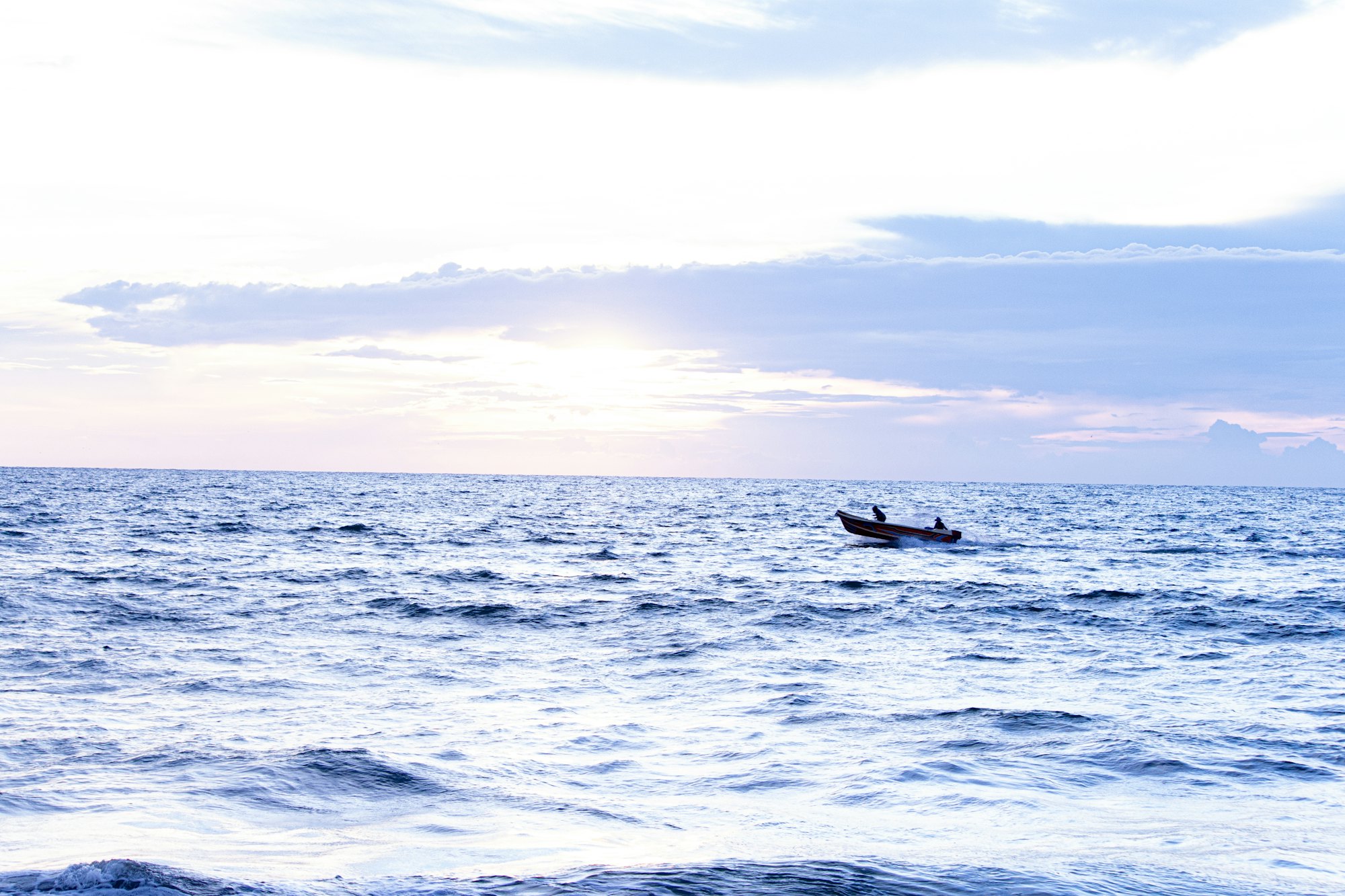 The pale blue sea off Negombo at dawn, with a single small fishing boat on the horizon.