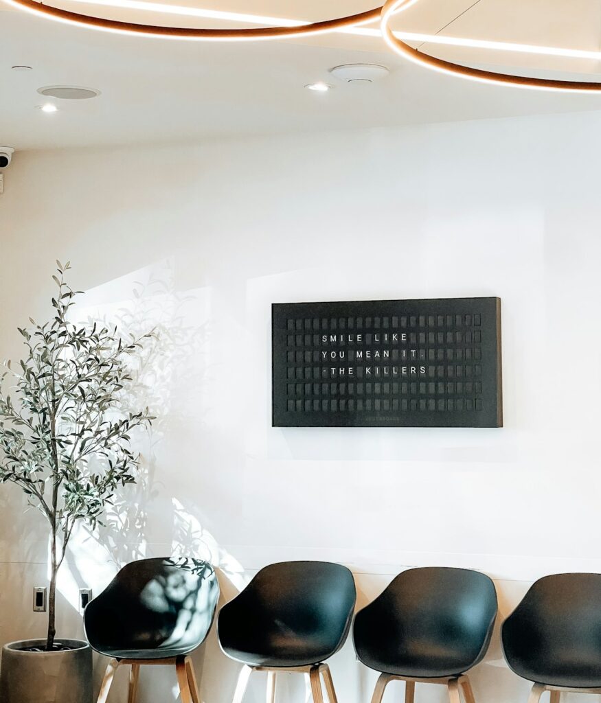 The waiting area: pale walls, a row of simple chairs and a potted olive tree.